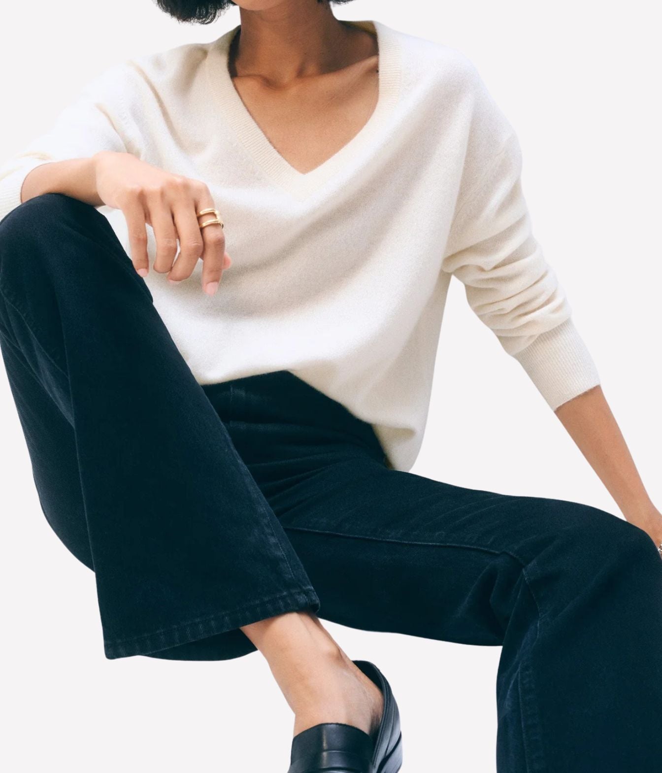 A person seated against a light neutral background, wearing a cream V-neck knit sweater