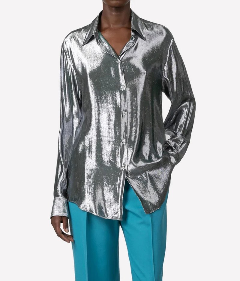 A model wearing a metallic silver long-sleeve button-up shirt and bright teal wide-leg trousers, shown against a plain light gray background.