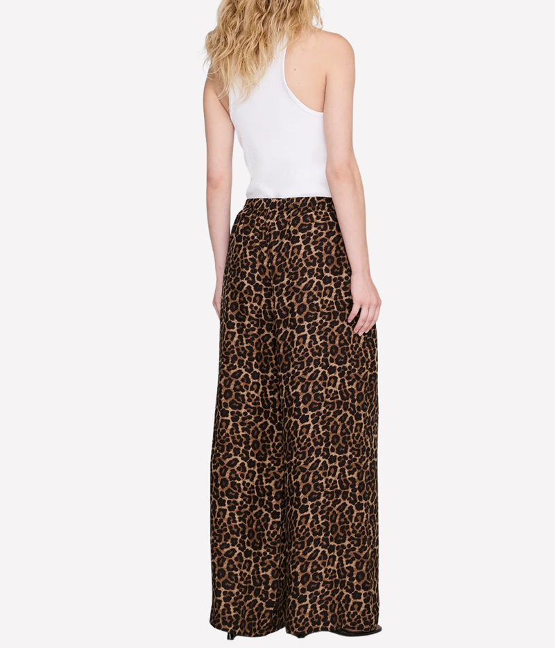 A woman shown from the back wearing leopard-print wide-leg pants and a white tank top against a plain light gray studio background.