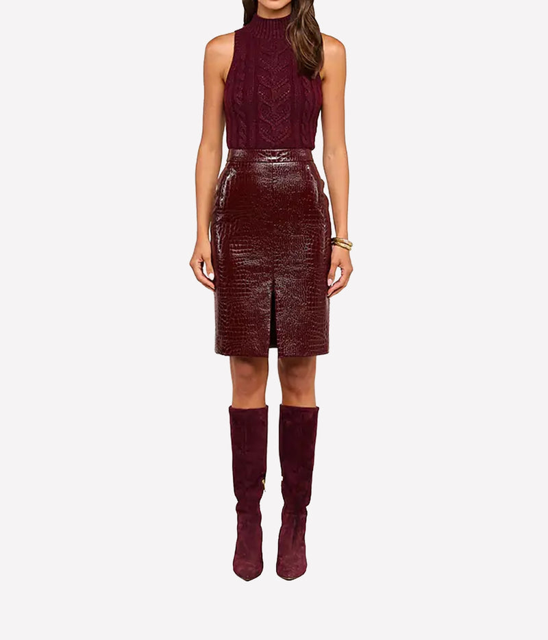 A model wearing a sleeveless high-neck burgundy knit top and a matching textured croc-embossed vegan leather skirt, paired with matching burgundy over-the-knee boots.