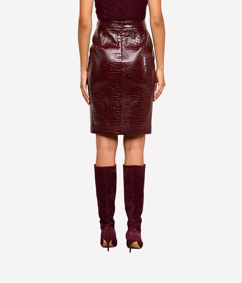 A model shown from the waist down wearing a glossy, dark burgundy croc-embossed vegan leather pencil skirt with matching burgundy suede over-the-knee boots
