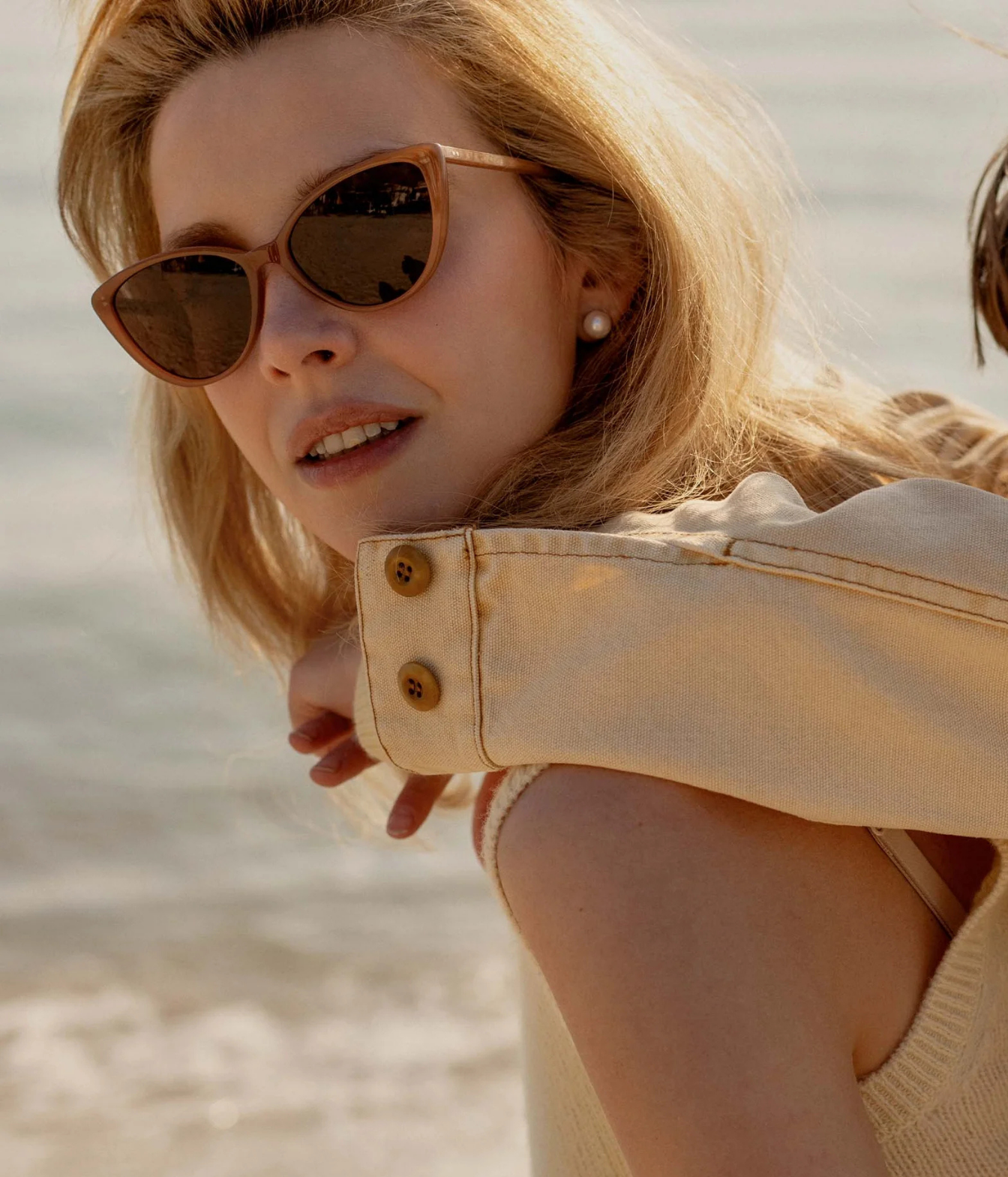 A close-up lifestyle shot of a woman wearing cat-eye sunglasses with brown frames and dark lenses