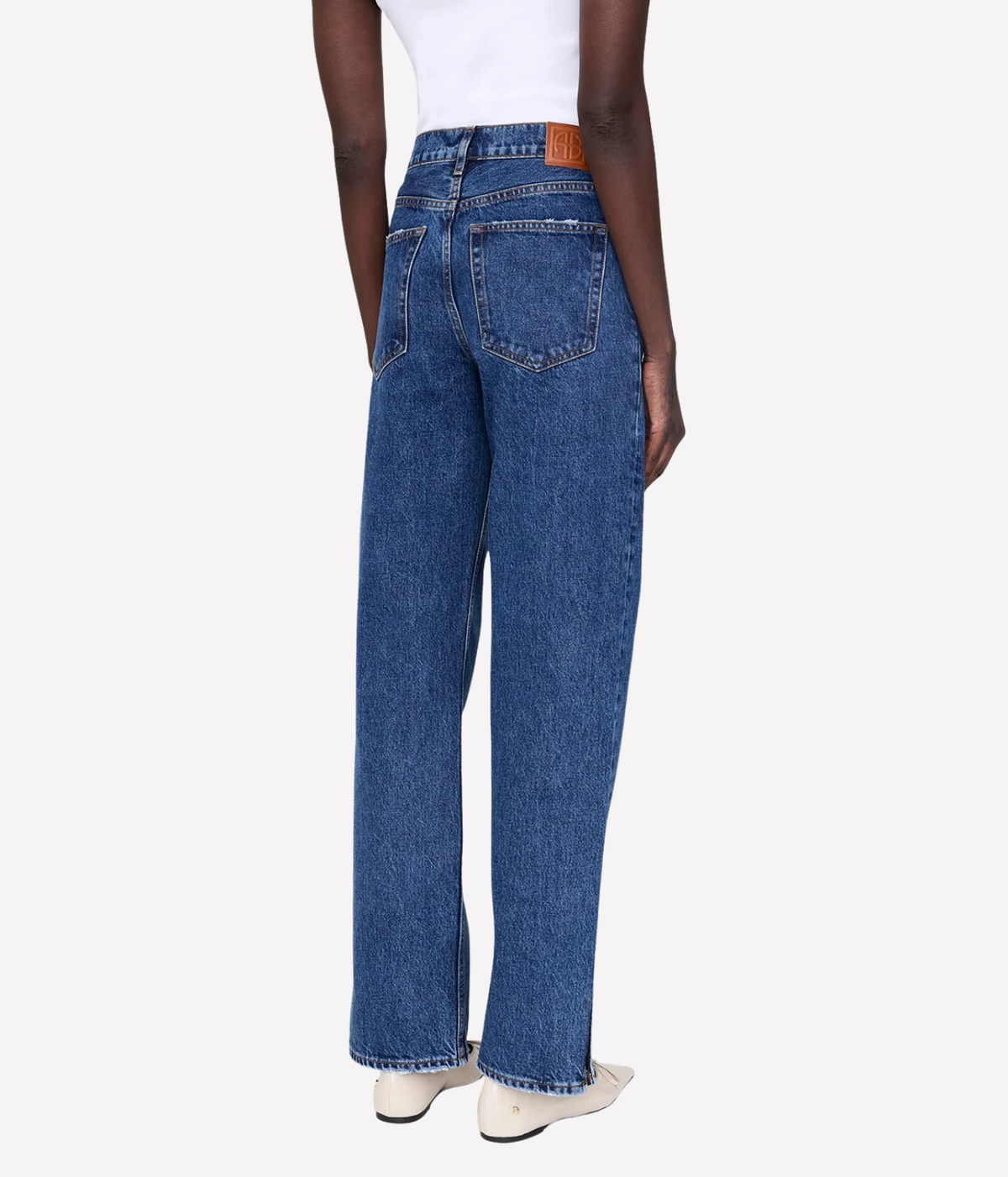 A model shown from the back wearing a pair of high-waisted, wide-leg blue denim jeans with a white top and white shoes, set against a plain light gray background.