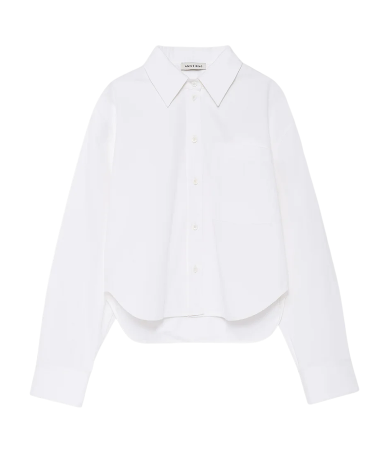 A white long-sleeve button-up shirt with a pointed collar, single chest pocket, and a relaxed cropped silhouette, shown on a plain white background.