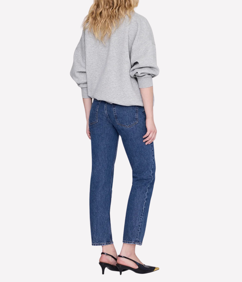 A woman shown from the back wearing a light gray oversized sweatshirt, blue cropped jeans, and black slingback heels against a plain light gray studio background.