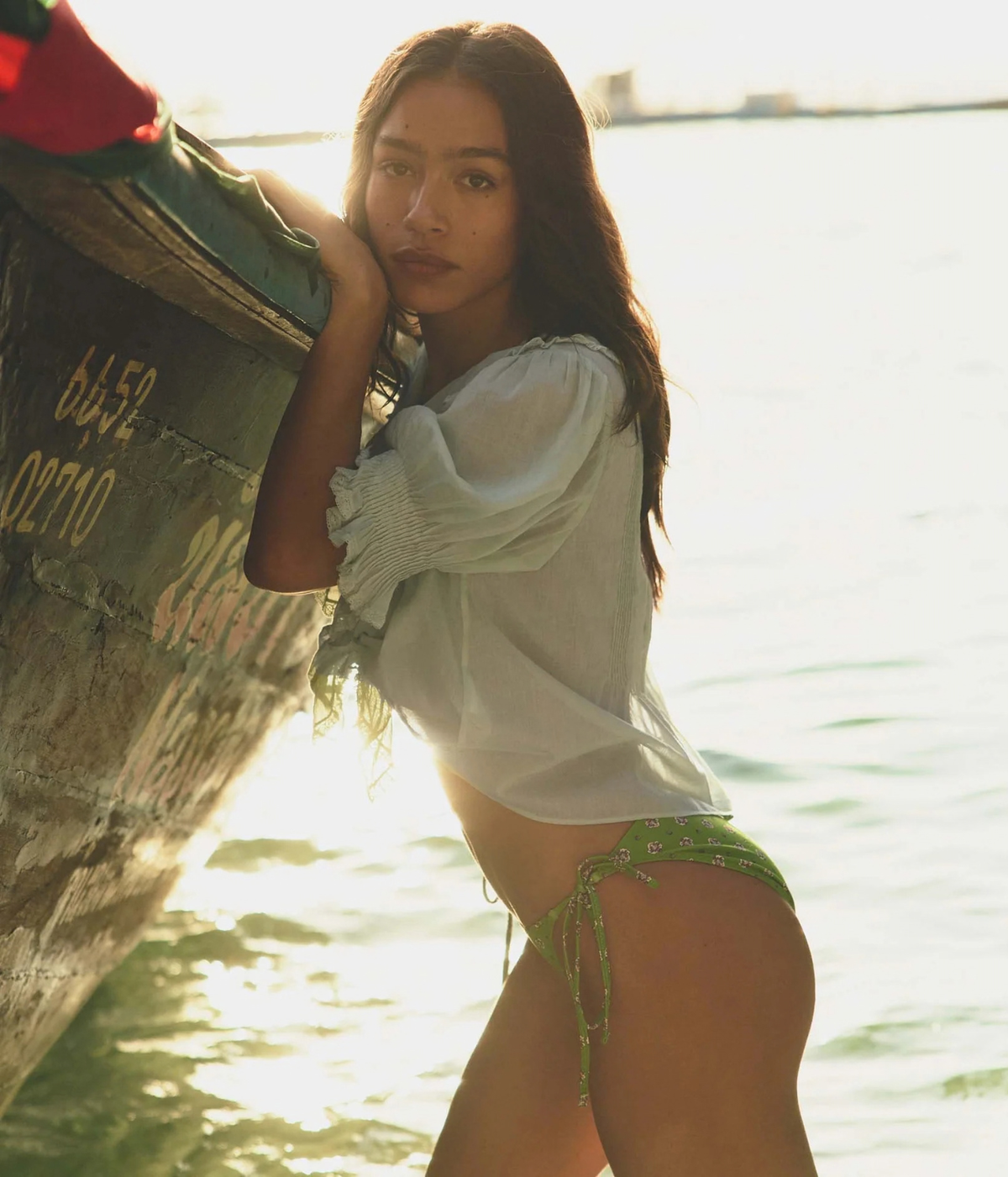 DÔEN Henri Top in Seafoam, side view on model leaning against a boat with the blouse tied at the front