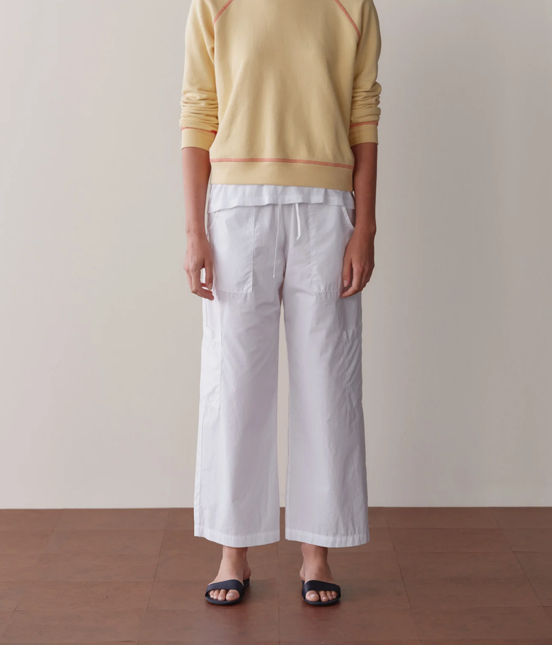 Front view of a model wearing the DONNI. The Pop Drawstring Cargo Pant in Powder with a pale yellow raglan sweatshirt with orange contrast stitching over a white tee and navy slide sandals