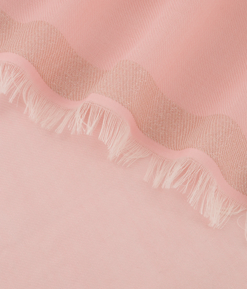 A close-up of a soft pink fabric with a scalloped edge and white fringe.
