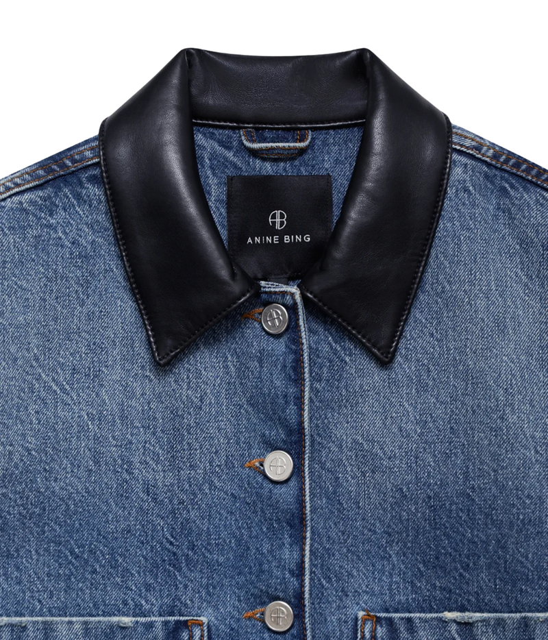 Close-up of a blue denim jacket with a contrasting black leather collar, featuring silver buttons and a visible Anine Bing brand label.