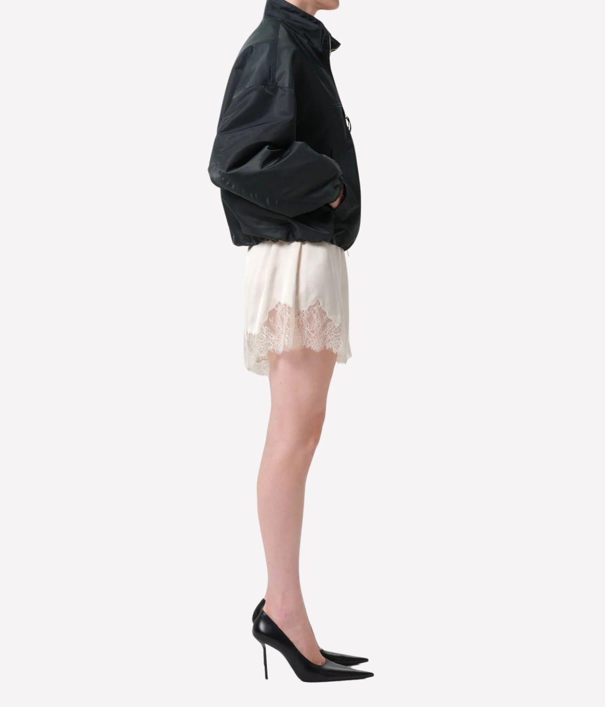 A model shown in profile wearing a black jacket, a cream lace-trimmed mini shorts - Lace Trimmed Tap Short in cream
