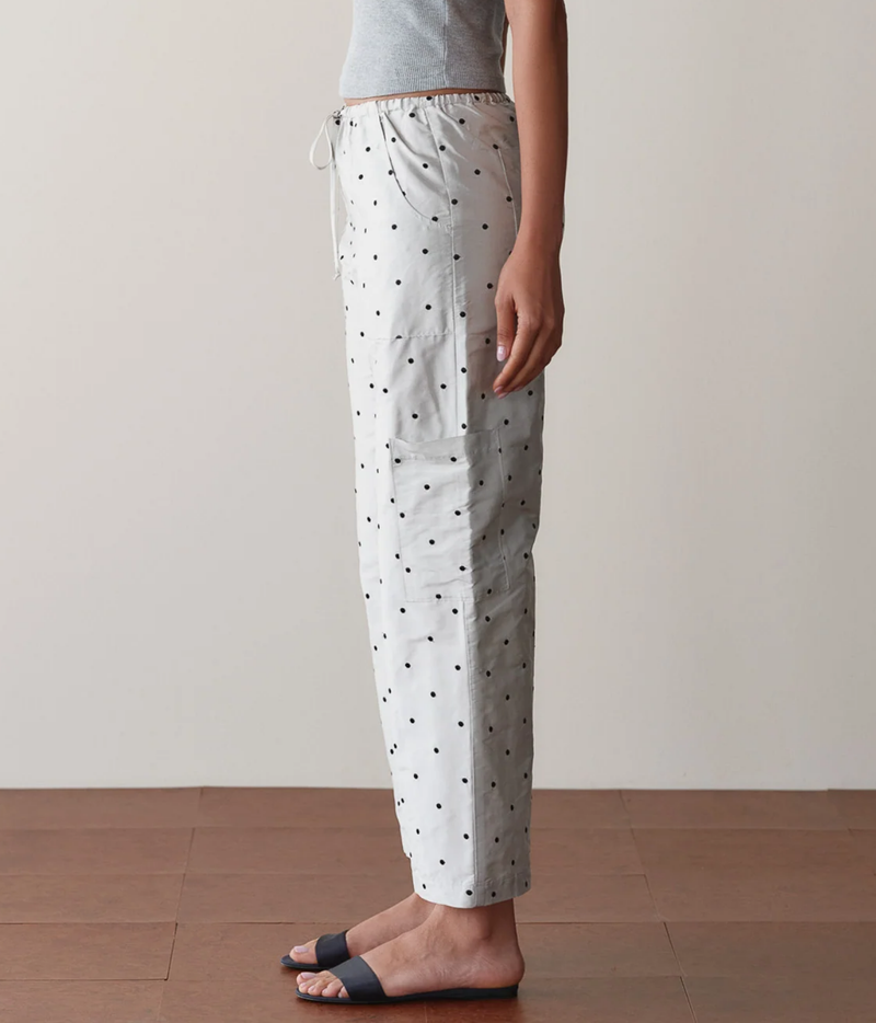 Side profile of a model wearing the DONNI. The Silk Taffeta Cargo Pant in Silver Polka Dot with a grey tank top and black slide sandals, showing the cropped length and relaxed straight leg