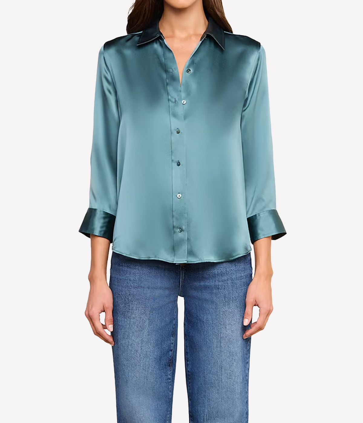 A woman wearing a cadet blue silk button-front blouse with contrasting dark collar and cuff trim, paired with blue jeans.