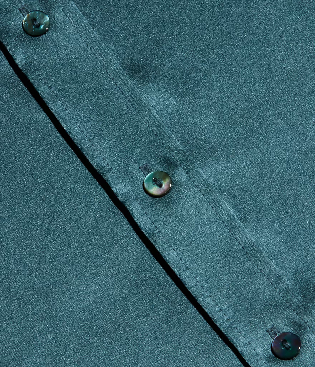 Close-up of a cadet blue silk fabric garment with a diagonal button placket and iridescent buttons.