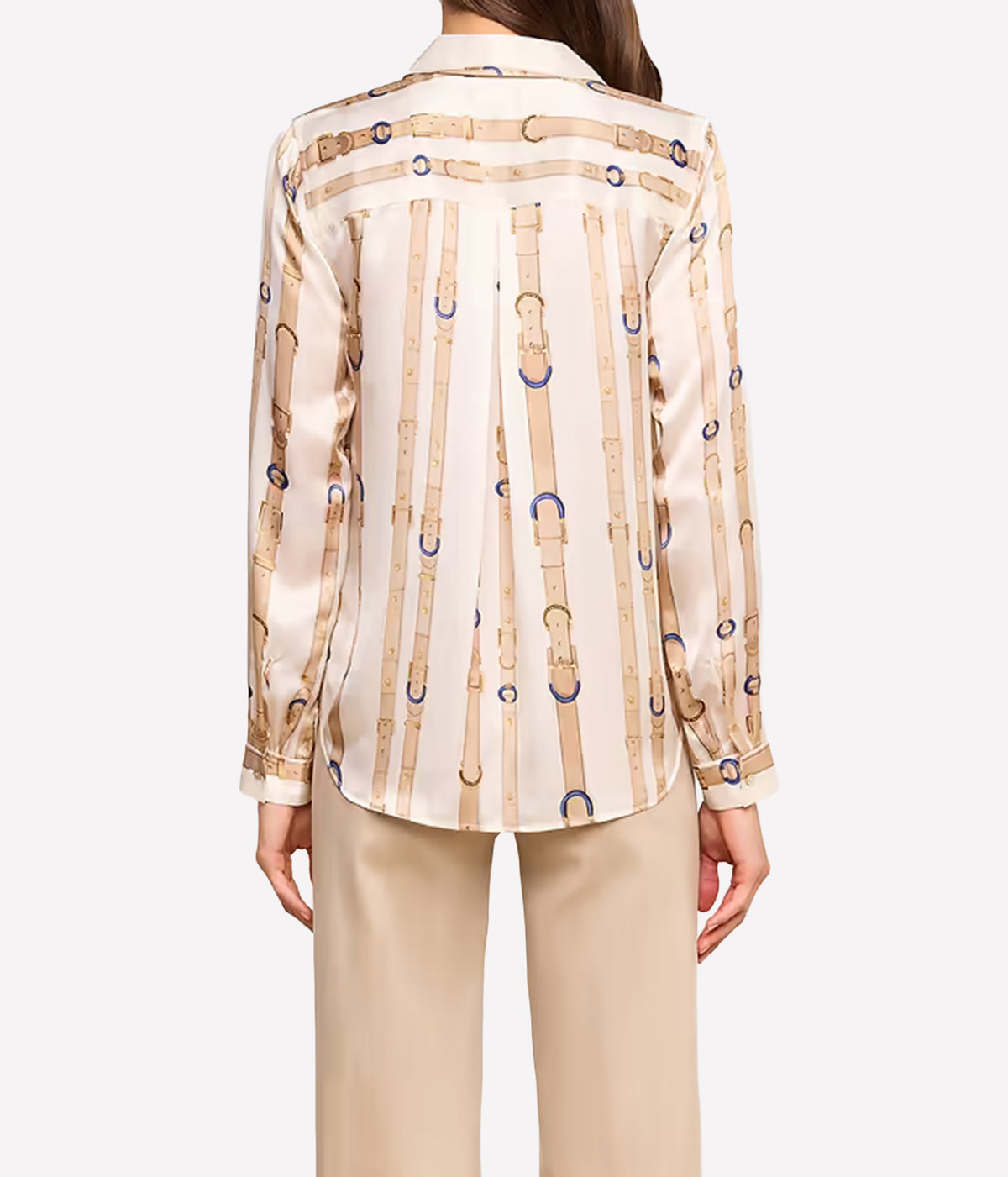 A woman shown from the back wearing a beige silk shirt with a vertical leather-buckle print in tan, gold, and blue, paired with beige trousers.
