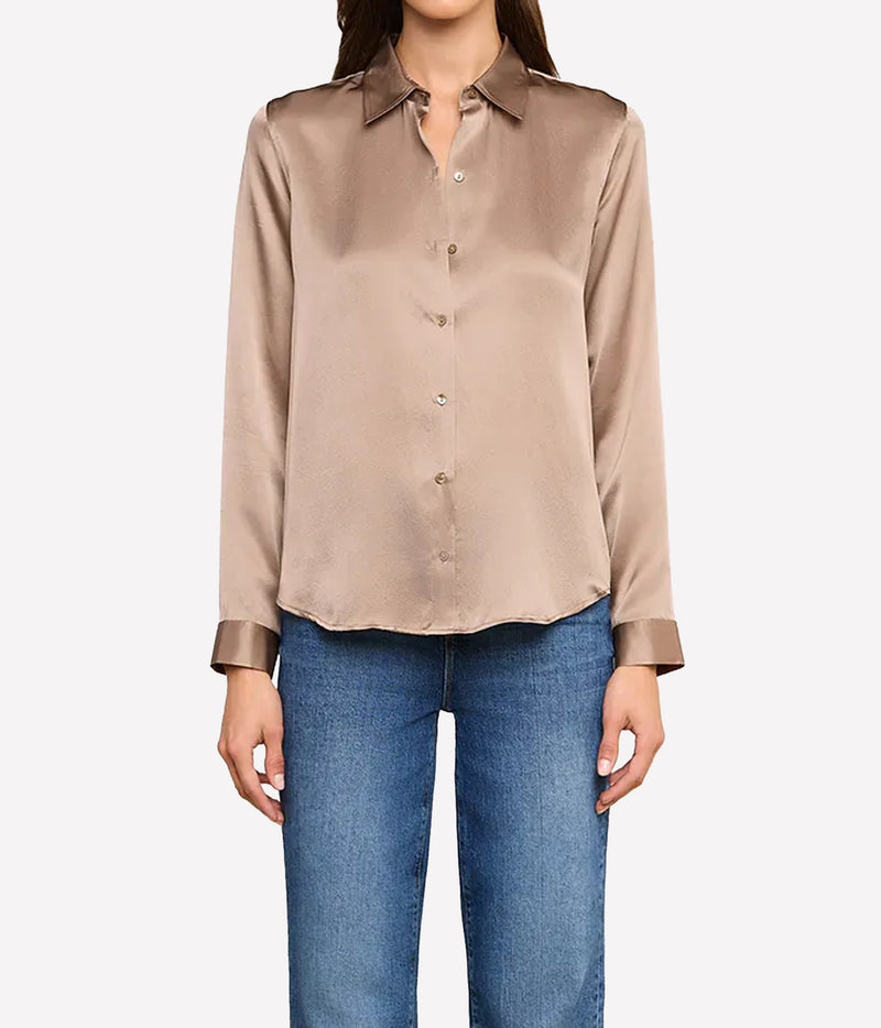A woman wearing a long-sleeve silk button-up blouse in a taupe-brown colour, paired with blue jeans.