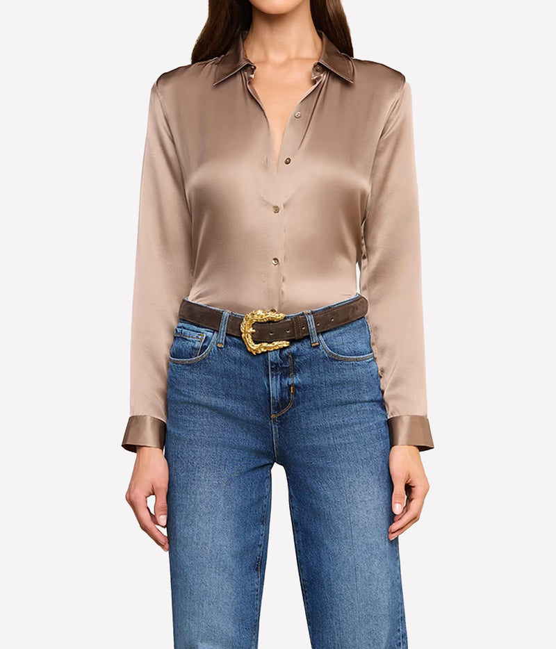 A woman wearing a long-sleeve silk button-up blouse, tucked into blue jeans with a dark brown belt featuring a gold buckle.