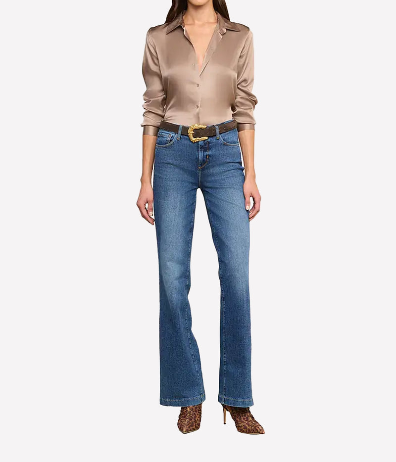 A model wearing a silk button-down shirt, blue high-rise flare jeans with a gold buckle belt, and leopard-print heels.