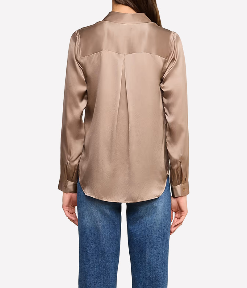 A woman viewed from the back wearing a long-sleeve silk blouse in a warm taupe colour, paired with blue jeans.