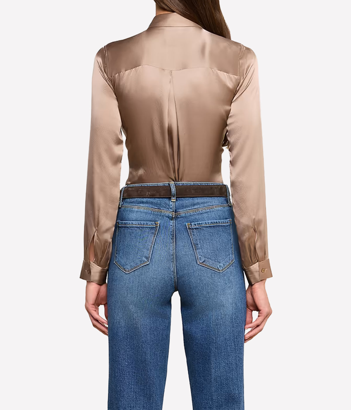 A woman shown from the back wearing a shiny taupe silk long-sleeve shirt tucked into blue jeans with a dark belt.