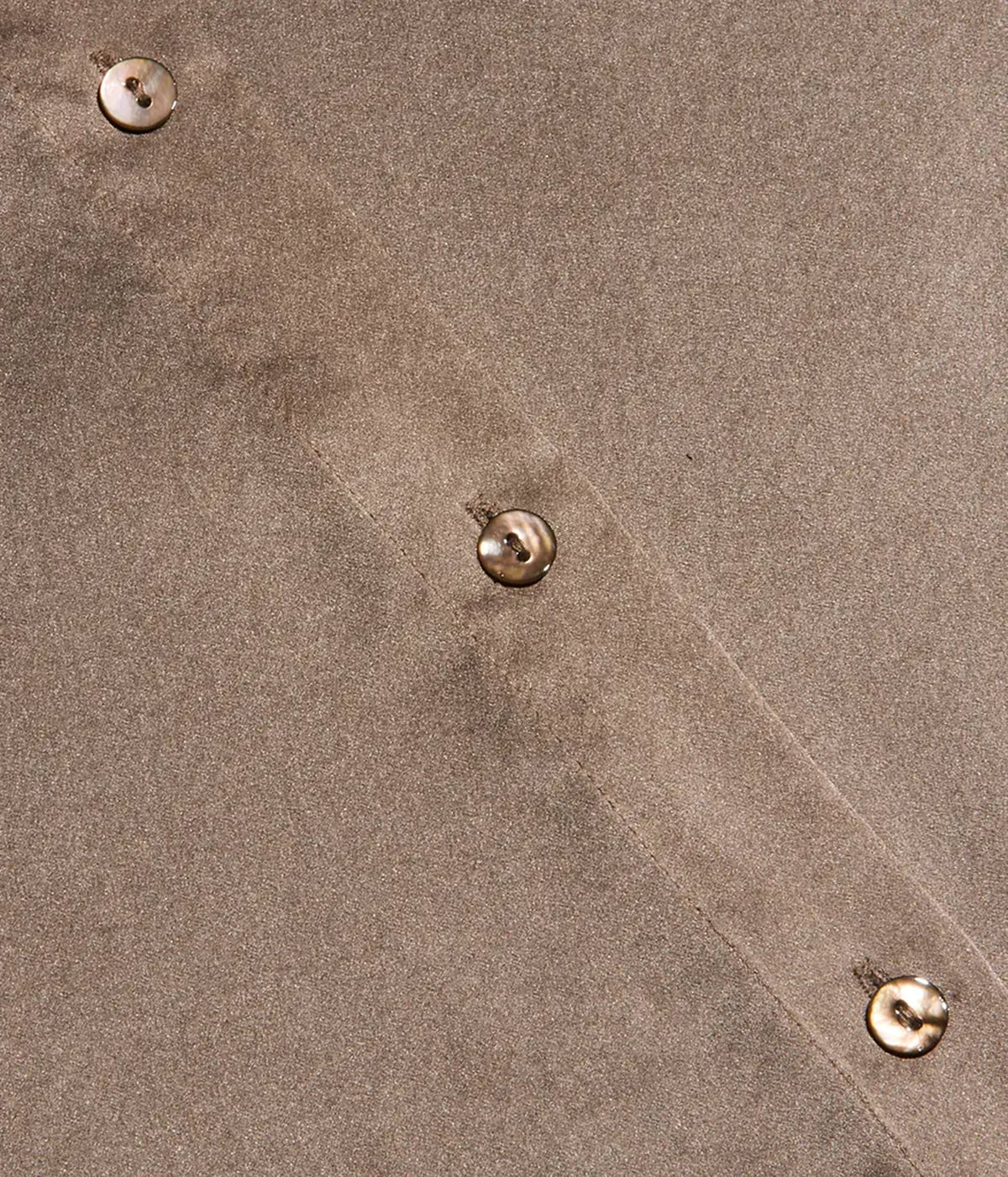 Close-up of a taupe-brown silk fabric surface with three visible metallic buttons spaced along a seam.