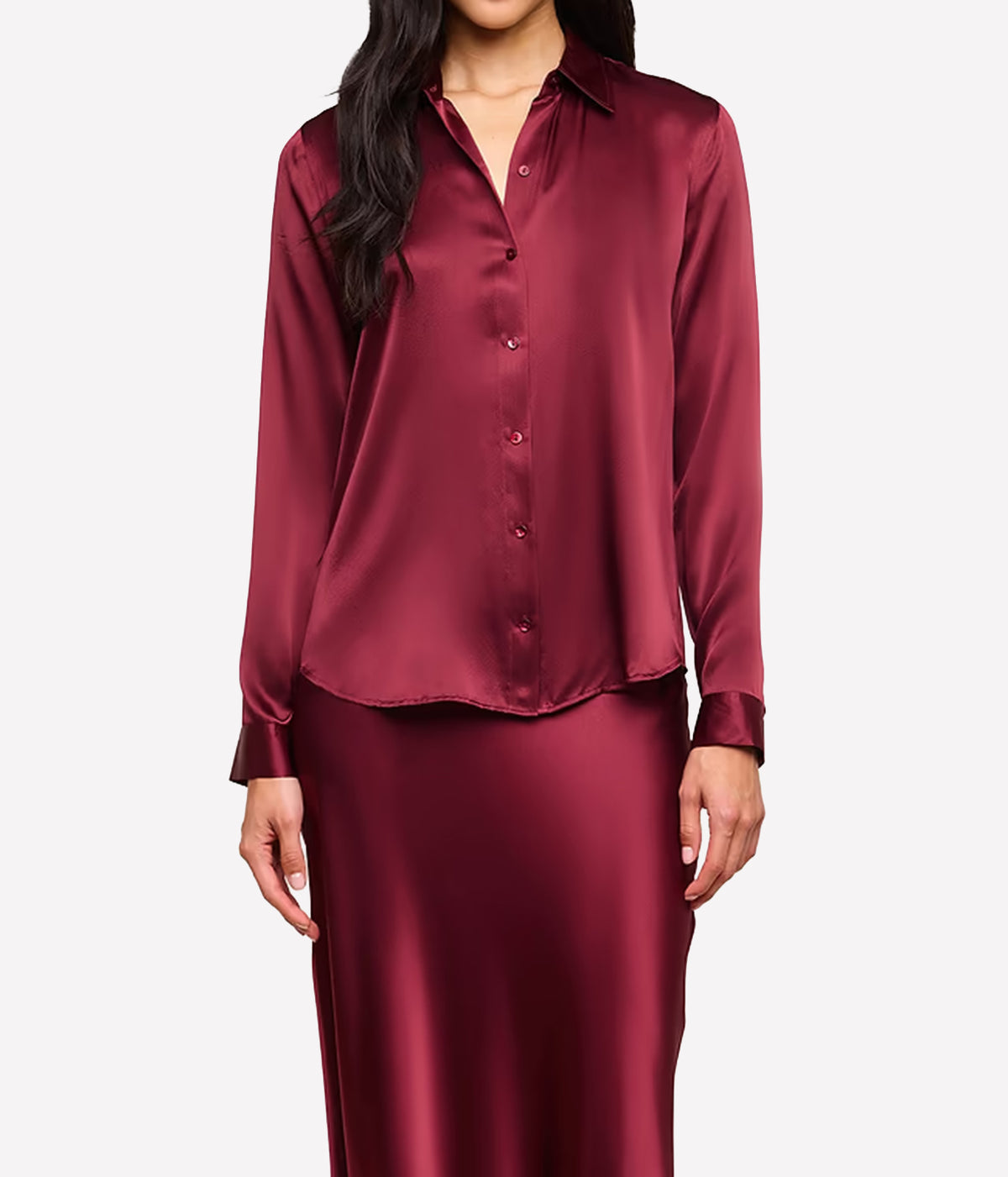 A front on view of a woman wearing the L'AGENCE Tyler Silk Blouse in Merlot Red, styled with a brown suede belt and matching silk maxi skirt in red