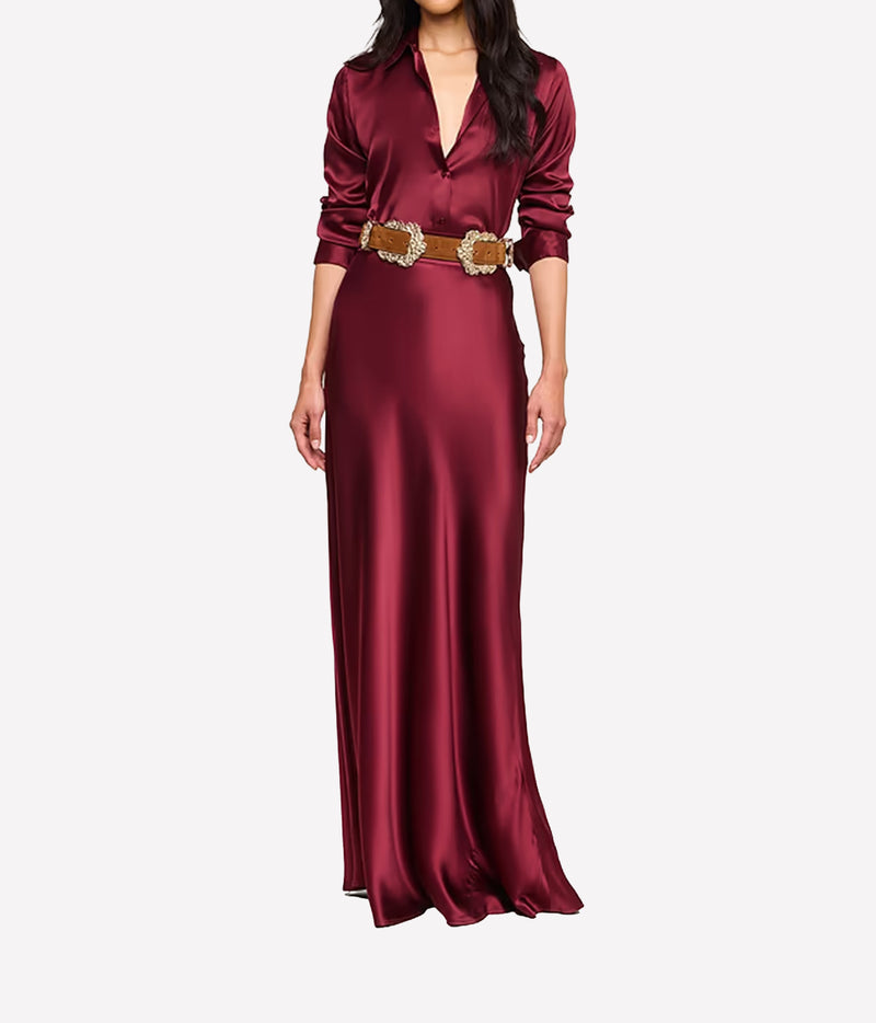 A woman wearing the L'AGENCE Tyler Silk Blouse in Merlot Red, styled with a brown suede belt and matching silk maxi skirt in red