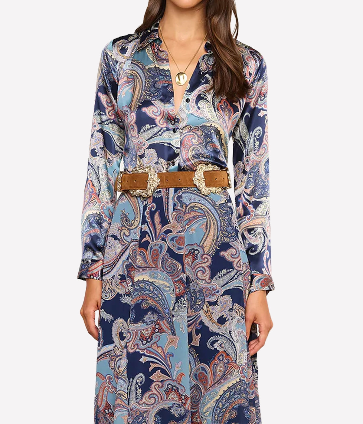 A woman wearing a long-sleeve button-front shirt with an intricate paisley print in navy, light blue, beige, and white, styled with a brown belt featuring large decorative gold-tone buckle details.
