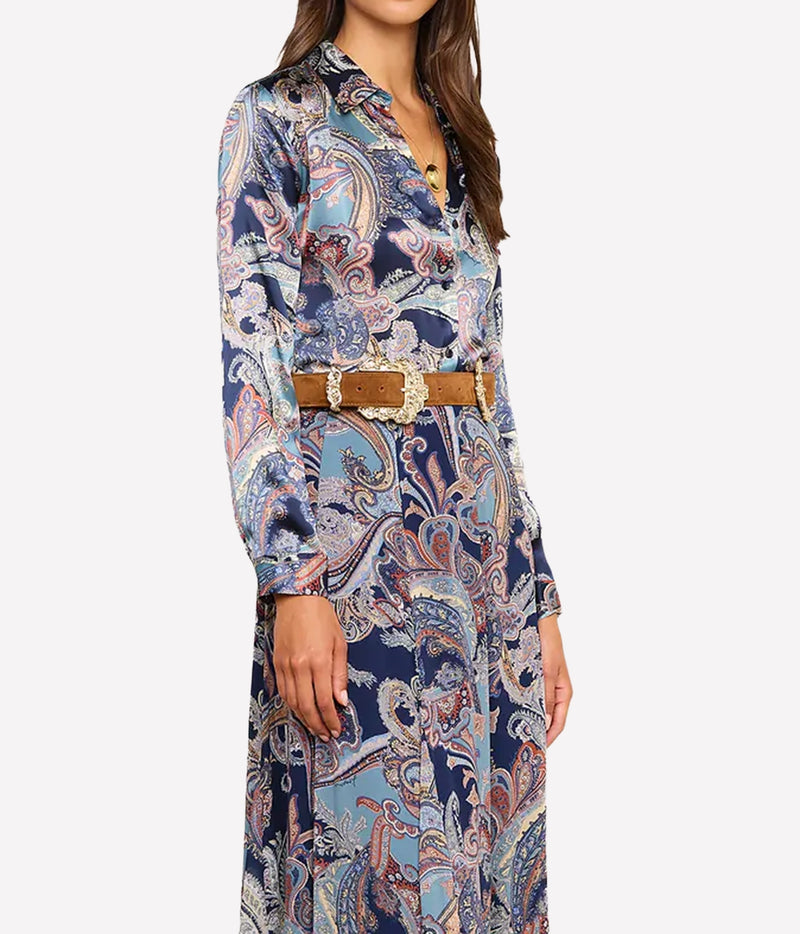 A woman wearing a long-sleeve collared shirt with an intricate paisley pattern in navy blue, light blue, beige, and white, styled with a brown belt featuring a large decorative buckle.