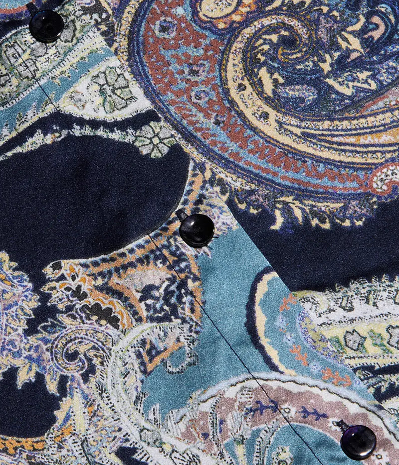 Close-up of a patterned button-up shirt fabric with a detailed paisley design in navy, teal, rust, cream, and gold, featuring black buttons.
