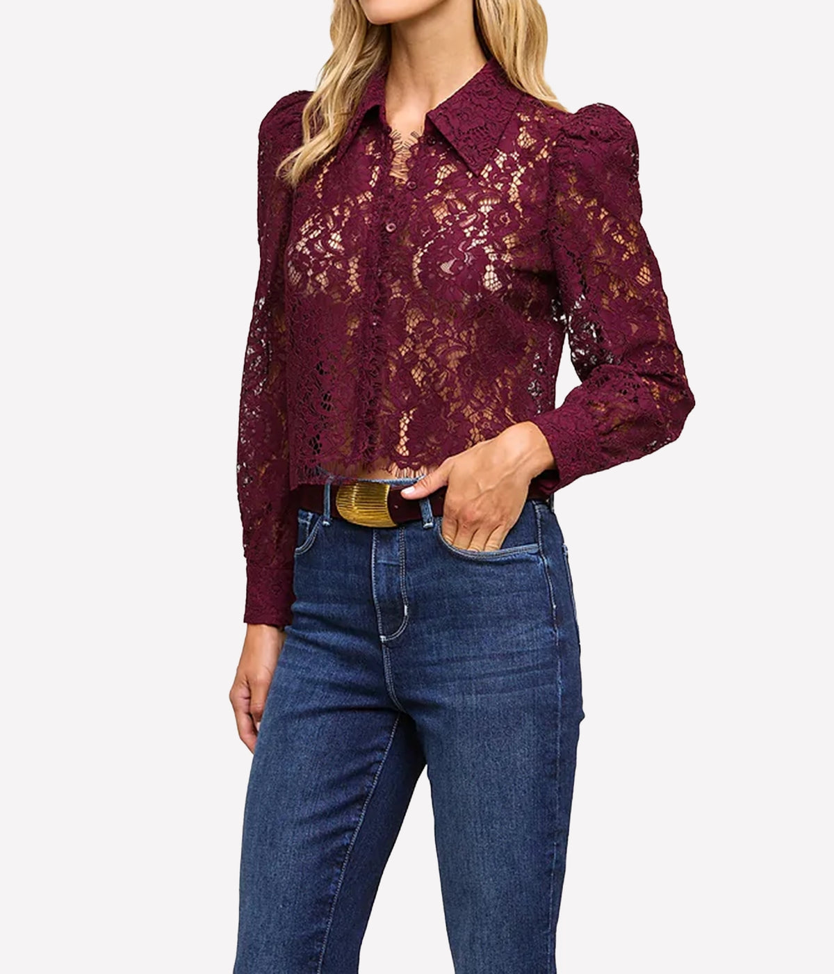 A woman wearing a burgundy lace long-sleeve blouse with puffed shoulders and blue jeans, shown from the neck down.