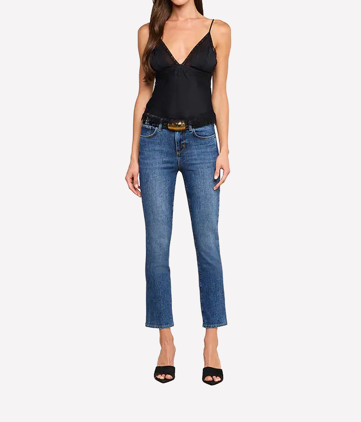 A model wearing the L'AGENCE Elka Satin Lace Camisole in Black, blue cropped jeans with a gold-tone belt, and black heeled sandals.
