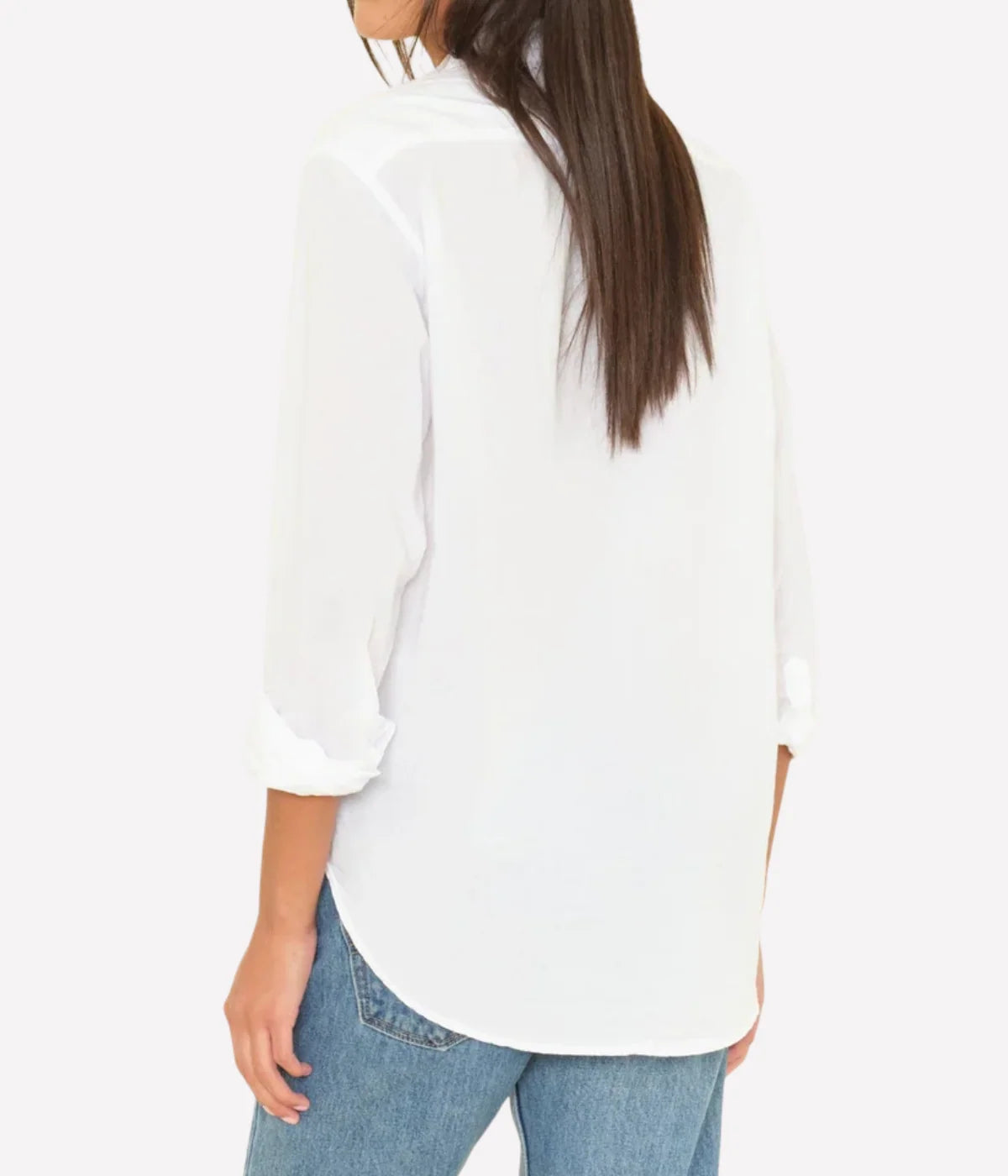 Back view of a model wearing the XiRENA Beau Shirt in White untucked over light-wash jeans, showing the relaxed oversized fit, rolled cuffs and curved shirttail hem