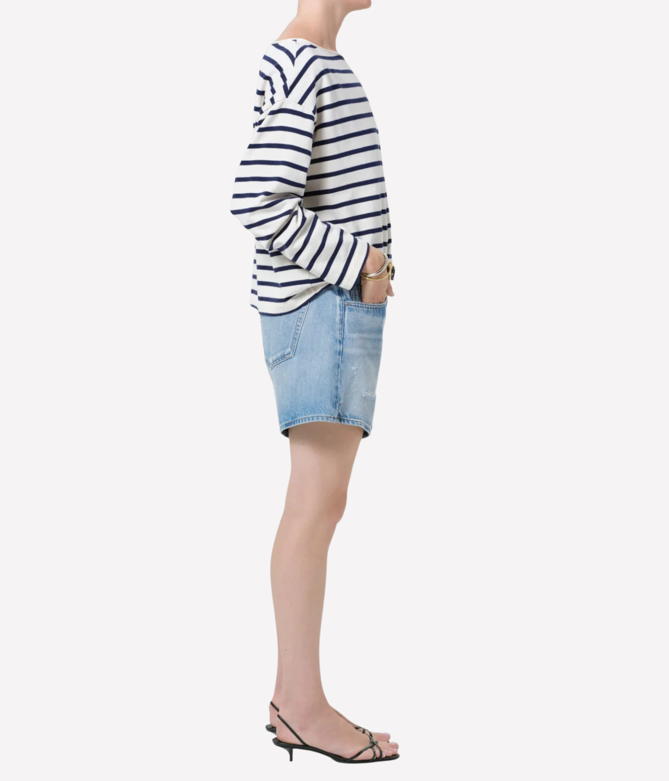 A model shown from the side wearing a navy and white horizontally striped long-sleeve top, a light blue denim mini skirt, and black strappy sandals against a plain light gray background.