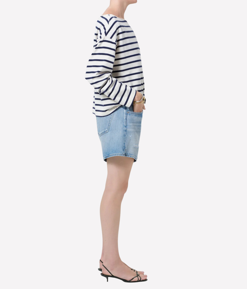 A model shown from the side wearing a navy and white horizontally striped long-sleeve top, a light blue denim mini skirt, and black strappy sandals against a plain light gray background.