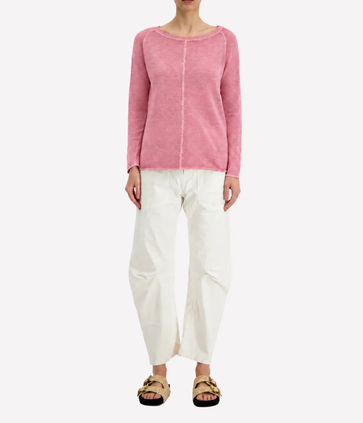 Front view of a model wearing the Avant Toi Maglia Pullover In Rose Skin untucked over cream barrel-leg trousers with dark sandals, showing the raglan sleeves and relaxed fit