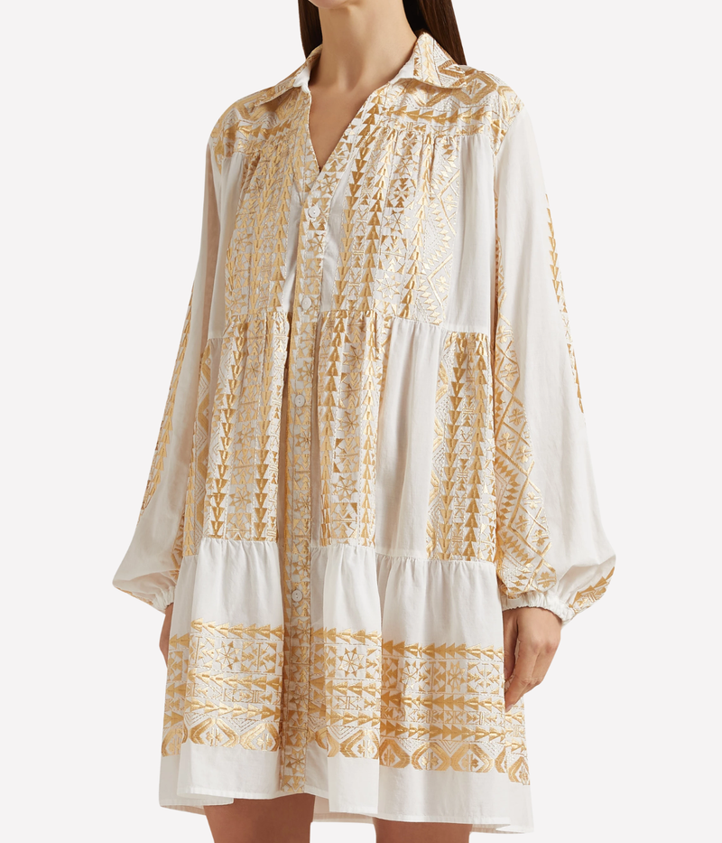 Front view of a model wearing the Greek Archaic Kori Short Classic Triangle Balloon Sleeve Shirt In White Gold as a relaxed mini dress, showing the open collar, gathered balloon sleeves and gold embroidered tiers.