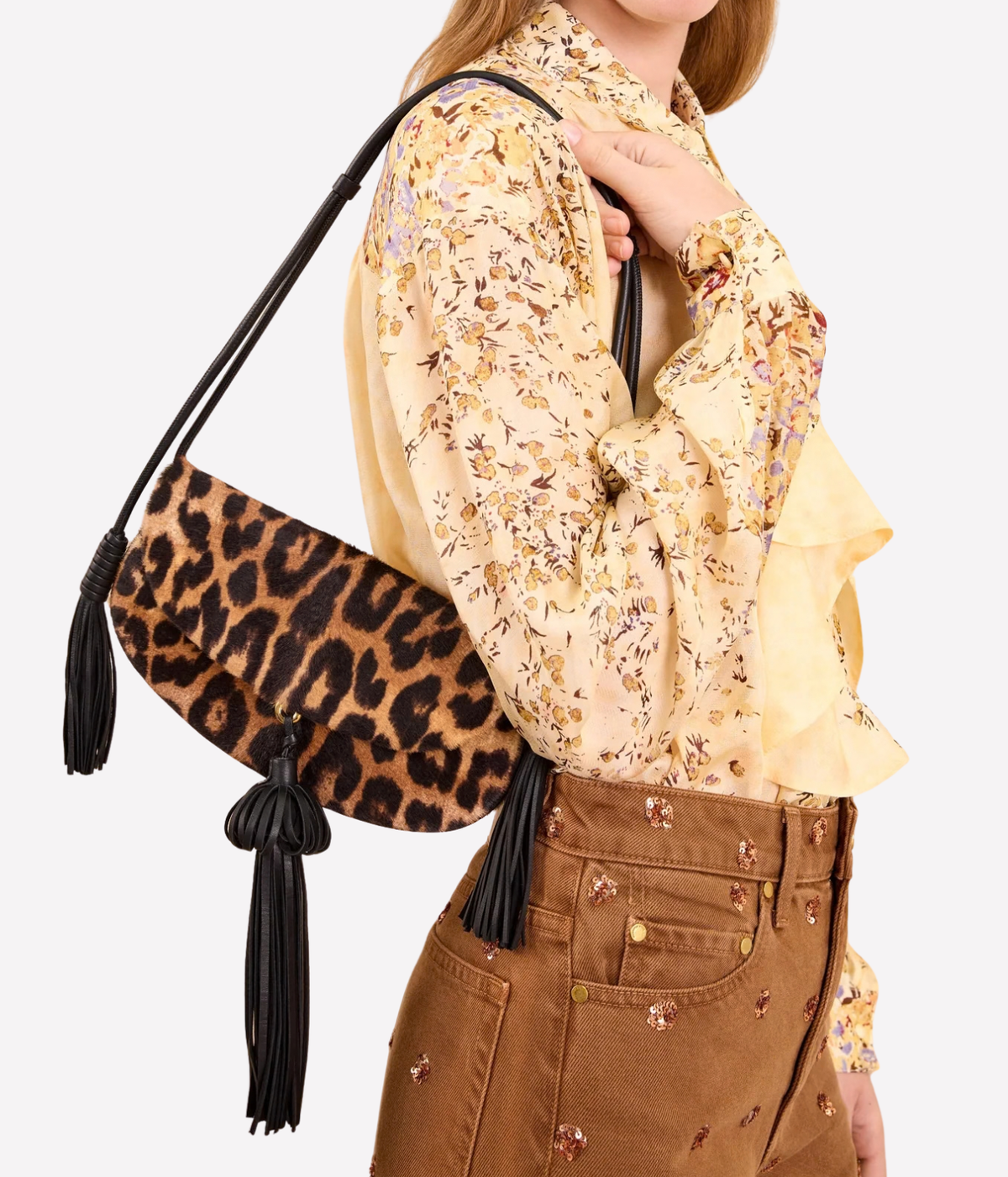 A model wearing a beige floral blouse and brown pants carries a leopard-print shoulder bag Paloma Flap Tassel Bag In Leopard