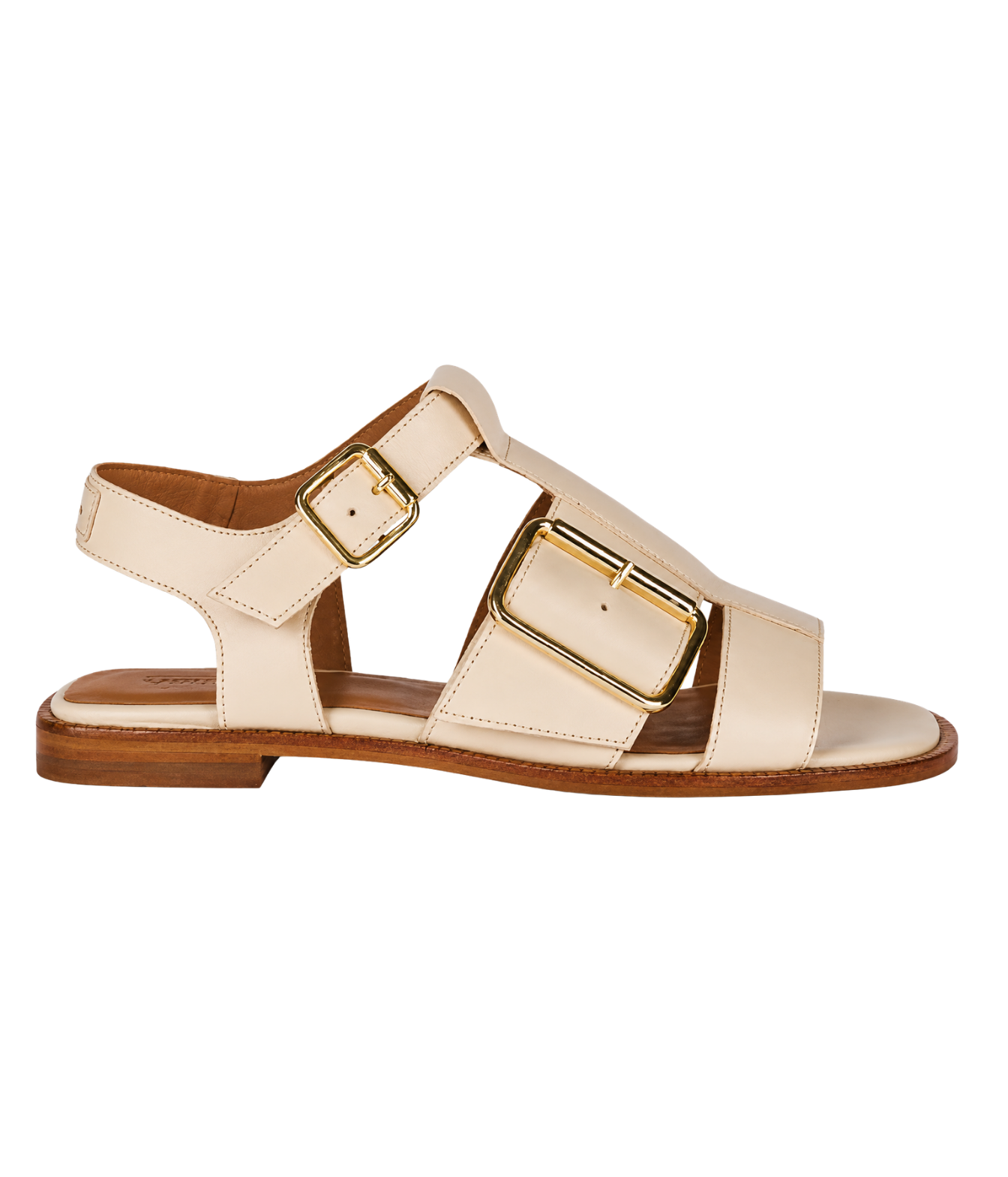 A single flat sandal in cream-colored leather with gold-tone metal buckles and a brown sole, shown in a side profile on a white background.
