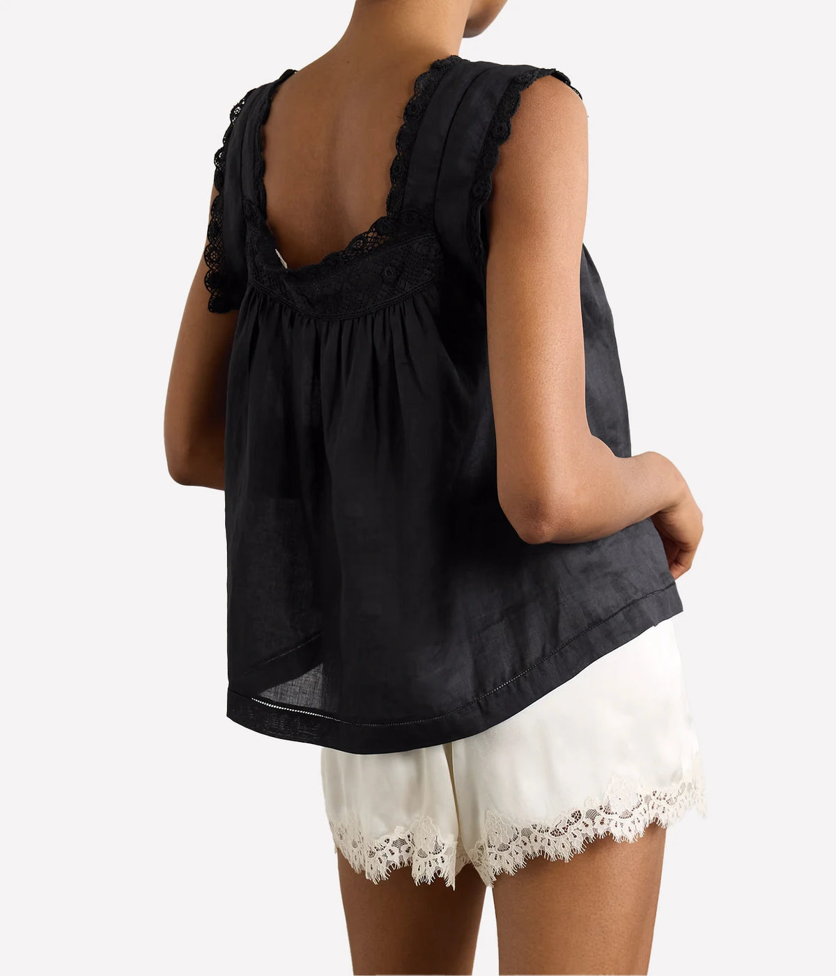 A woman shown from the back wearing a black sleeveless top with lace trim and white shorts against a plain light background.