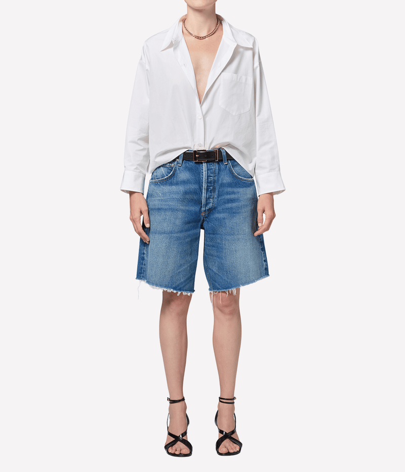 Model wearing the Citizens of Humanity Ayla Short in Chaya with a white shirt open at the collar and sleeves pushed up, a black leather belt, a gold necklace and black strappy heeled sandals