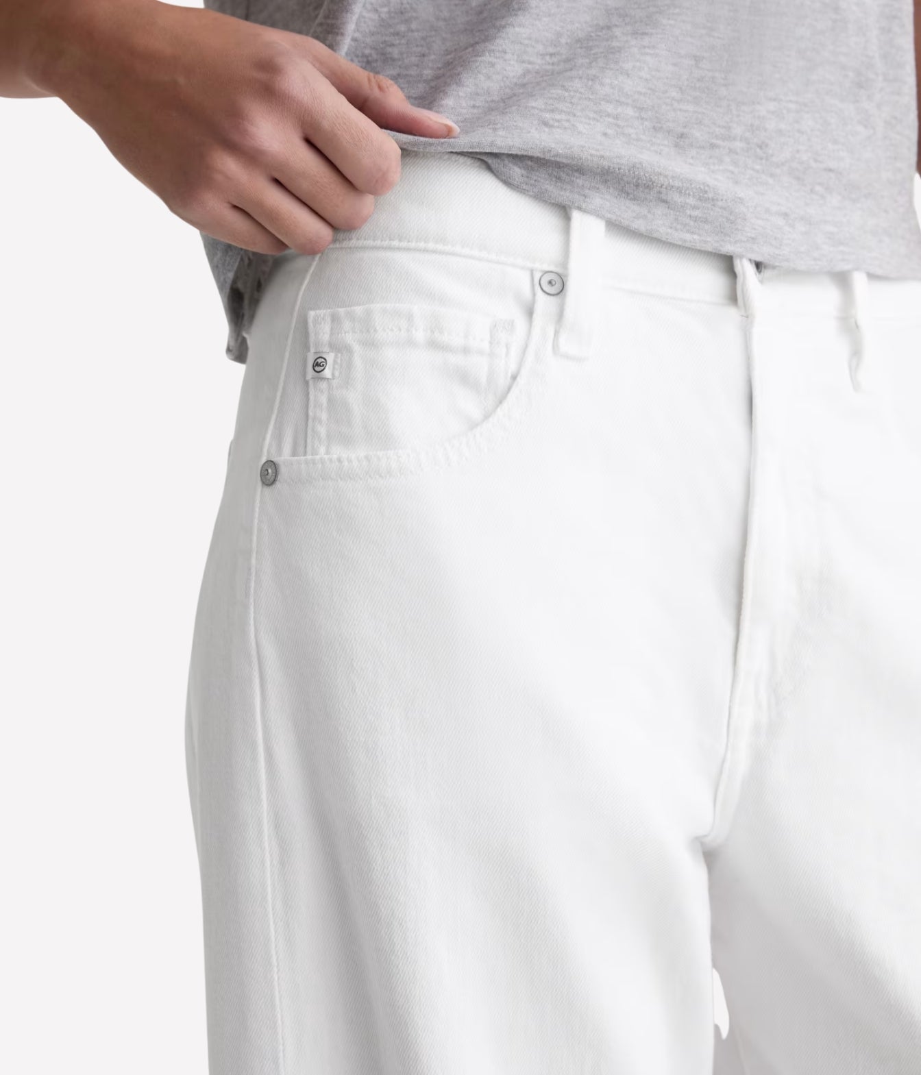 Close-up of a person wearing white denim jeans, showing the back pocket, button, waistband, and part of a light gray heathered t-shirt.