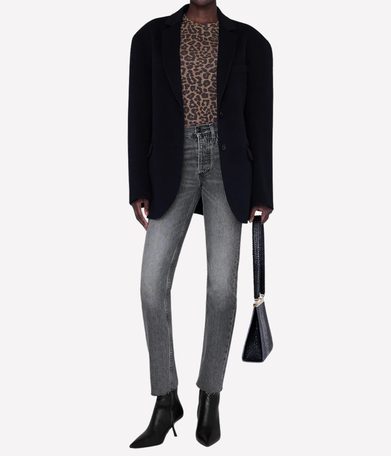 A model is shown from the neck down wearing a black blazer, a brown and black leopard print top, gray skinny jeans, and black pointed-toe ankle boots, while holding a black handbag against a light gray background.