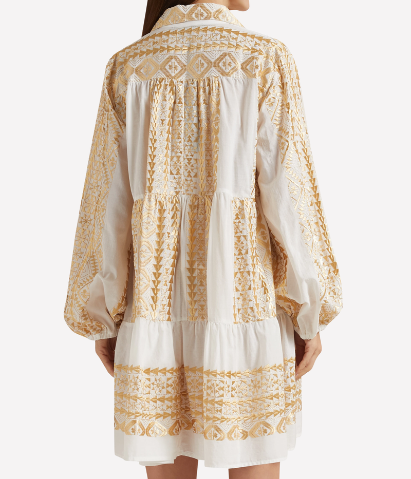 Back view of a model wearing the Greek Archaic Kori Short Classic Triangle Balloon Sleeve Shirt In White Gold, showing the gold embroidered yoke, gathered balloon sleeves and tiered hem.