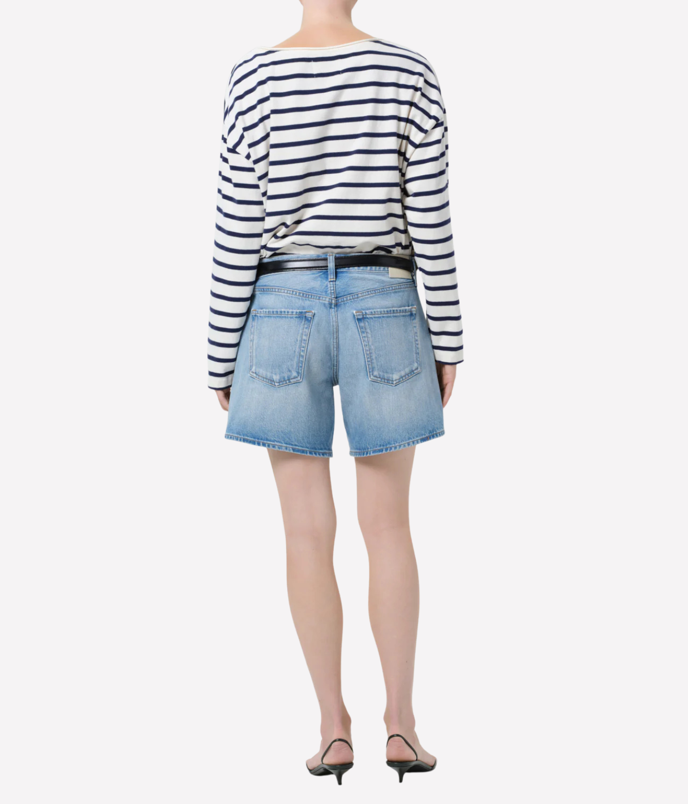 A model shown from the back wearing a navy and white horizontally striped long-sleeve top, light blue denim shorts, a black belt, and black pointed-toe heels against a plain white background.