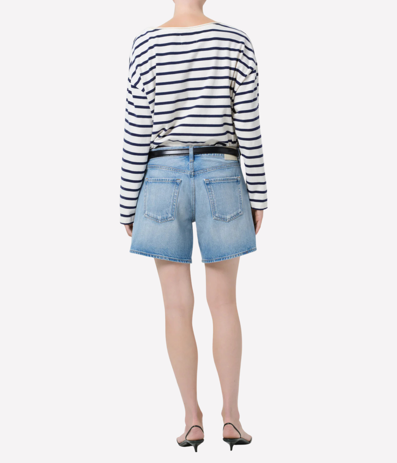 A model shown from the back wearing a navy and white horizontally striped long-sleeve top, light blue denim shorts, a black belt, and black pointed-toe heels against a plain white background.