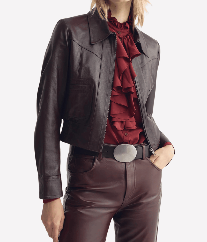 Model wearing the Nili Lotan Charly Leather Jacket in Bordeaux open over a red ruffled blouse with matching leather trousers, a black belt with a silver oval buckle and one hand in pocket