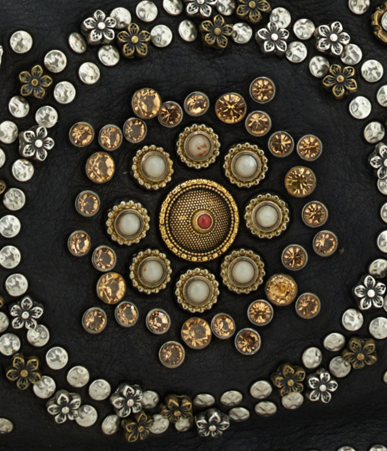 A close-up of an ornate circular decorative arrangement of vintage-style buttons and embellishments on a dark textured background. 