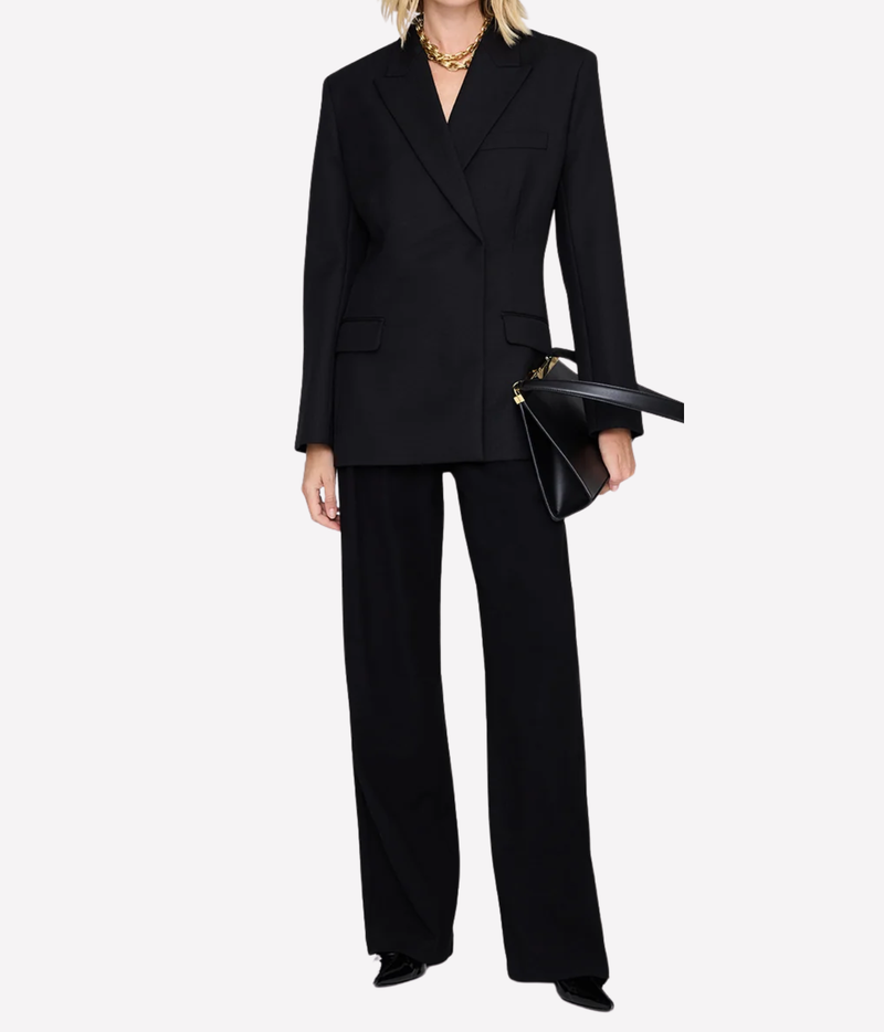 Model wearing the Anine Bing Aretha Blazer in Black buttoned with matching black wide-leg trousers, gold necklace and a black leather bag under the arm