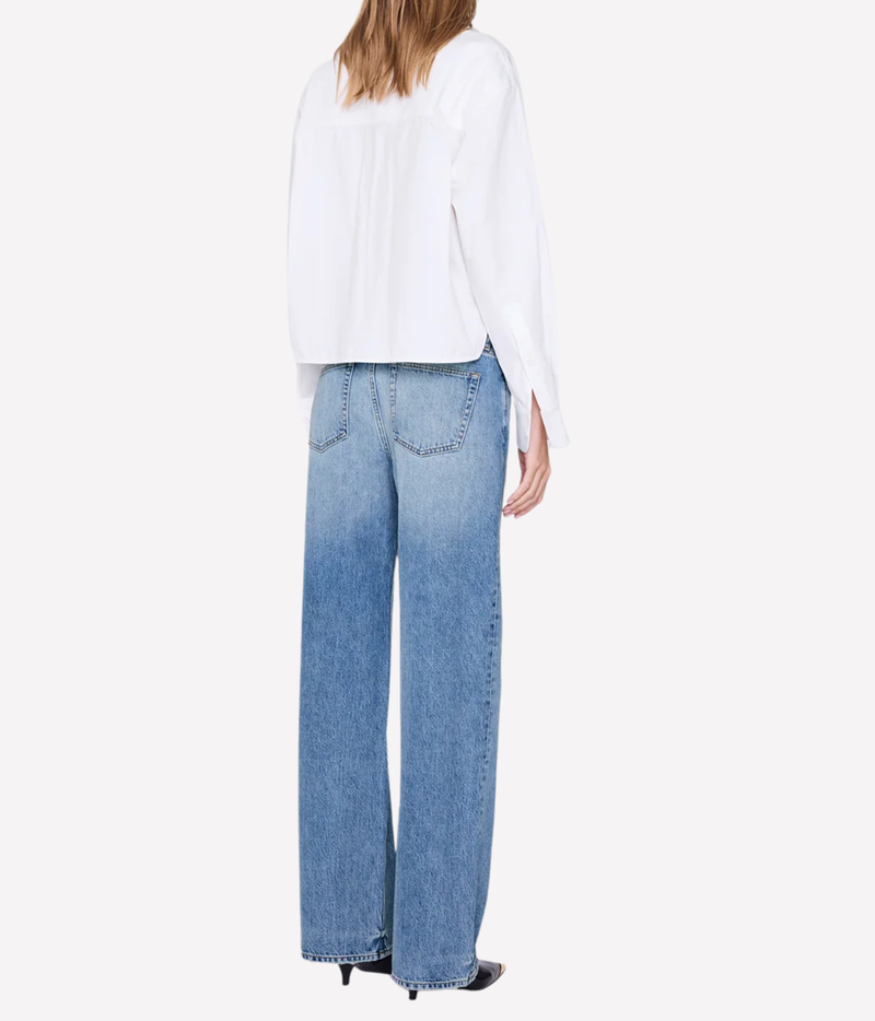 A model shown from the back wearing a white long-sleeve blouse and light blue wide-leg denim jeans, set against a plain white studio background.