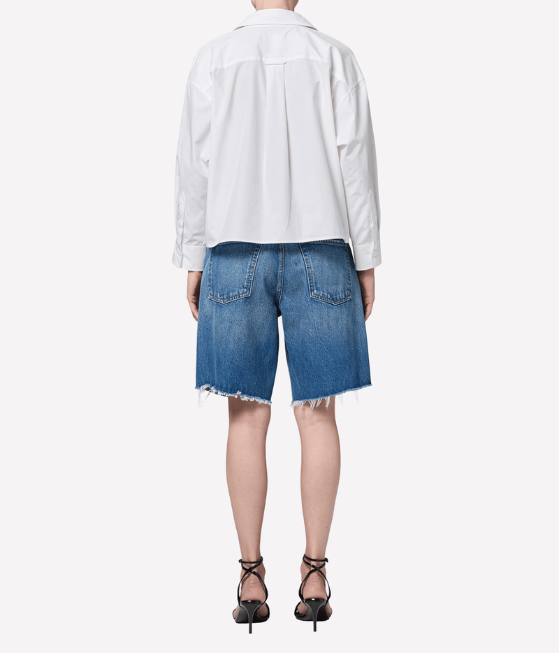 Back view of a model wearing the Citizens of Humanity Ayla Short in Chaya with a loose white shirt and black strappy heeled sandals, showing the back pockets and frayed raw hems